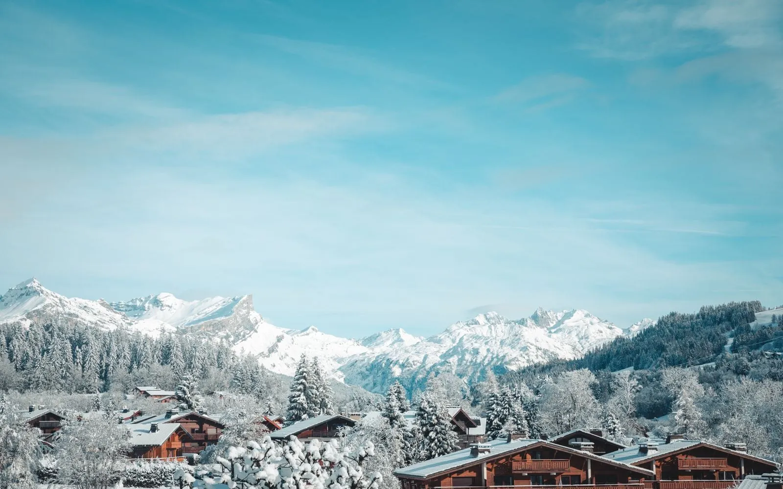 Des chalets de bois enneigés à Megève, des sapins givrés et des sommets sous un ciel bleu.